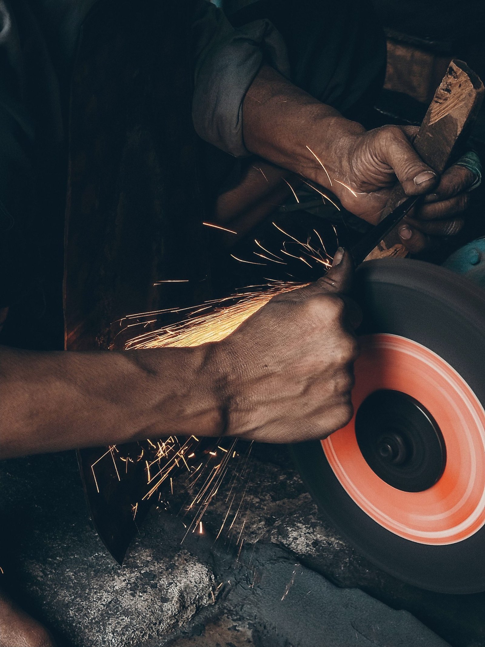 A part held against a spinning abrasive wheel, sparks flying.