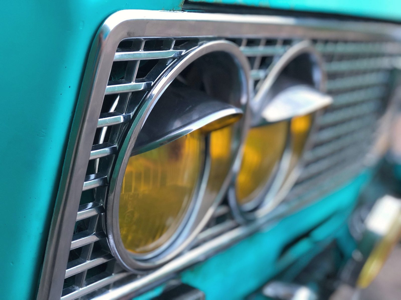A chrome headlight surround on a turquoise vintage car.
